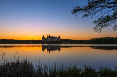 Alacakaranlıktaki Moritzburg Kalesi 'nin panoramik ve simetrik görüntüsü. Gökyüzü tepedeki maviden ufuktaki yoğun bir portakala dönüşür..