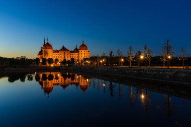Moritzburg Kalesi 'nin büyüleyici bir alacakaranlık görüntüsü. Barok kalesinin dışı sıcak bir şekilde aydınlatılmış..