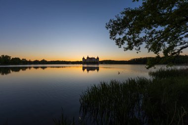 Alacakaranlıktaki Moritzburg Kalesi 'nin panoramik ve simetrik görüntüsü. Gökyüzü tepedeki maviden ufuktaki yoğun bir portakala dönüşür.