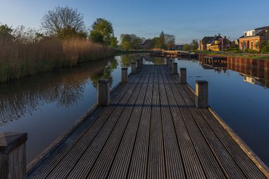 Bedum Kanalı 'nın üzerindeki ahşap bir iskelenin simetrik görüntüsü. Sabah güneşi, yansımalı sakin su ve tipik Hollanda rıhtım evleri..