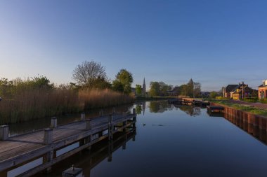 Hollanda, Bedum 'da ahşap iskeleli manzara kanalı. Sabah sakinliği, evlerin yansımaları ve ufuktaki Walfriduskerk kilise kulesi..
