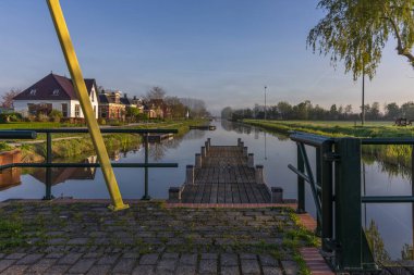 Bedum Kanalı 'nın asma köprüden sabah görüşü. Ahşap iskele, ev yansımaları ve tipik bir Hollanda köyünde sis..