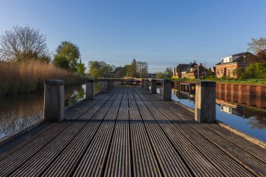Gün doğumunda Hollanda 'nın sakin bir köyünde sakin bir kanalda ahşap iskele. Geleneksel ev manzarası ve uzak bir kilise kulesi..
