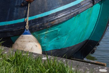 Beton iskelenin yanında demirli çamurluğu olan tarihi bir turkuaz tekne gövdesinin ayrıntıları. Groningen bölgesinden otantik denizcilik dokusu.