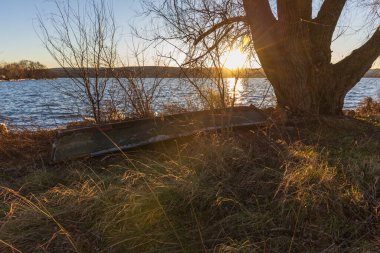Kırsal, terk edilmiş bir kayık, büyük bir söğüt ağacının dallarının altında, çimenli bir gölün kıyısında baş aşağı yatıyor. Sahne, batan güneşin yoğun altın parıltısıyla aydınlanır. Güçlü bir mercek parıltısı yaratır ve metni aydınlatır.