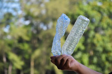 Boş plastik şişeler ve el altında bükülmüş plastik şişeler, küresel ısınmayı azaltma, kirliliği azaltma ve dünyanın dört bir yanındaki çevreyi kurtarma kavramı.