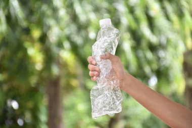Boş plastik şişeler ve el altında bükülmüş plastik şişeler, küresel ısınmayı azaltma, kirliliği azaltma ve dünyanın dört bir yanındaki çevreyi kurtarma kavramı.