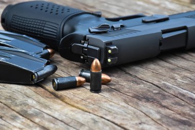 Otomatik siyah 9 mm 'lik tabanca, mühimmat ve mermiler ahşap masada. Silaha özel seçmeli odaklanma.
