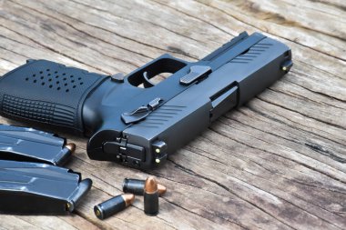 Otomatik siyah 9 mm 'lik tabanca, mühimmat ve mermiler ahşap masada. Silaha özel seçmeli odaklanma.