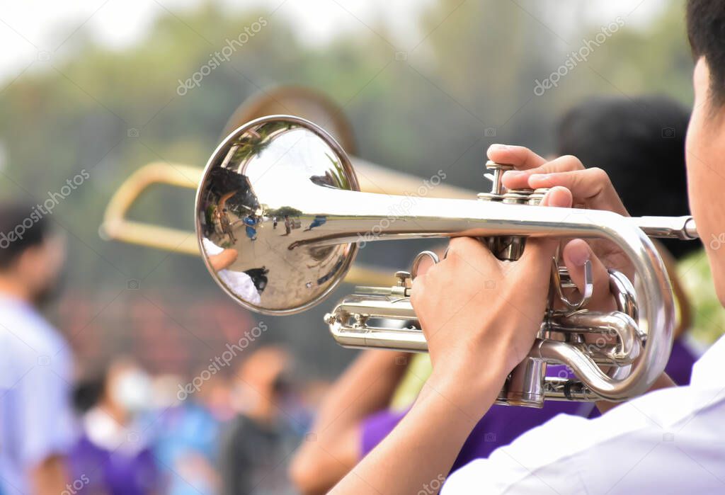 Asian young boy student blowing a trumpet with school marching band, blurred background, soft focus.
