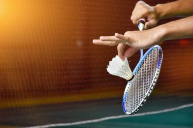 Badminton raketi ve eski beyaz mekikçik oyuncunun elinde tutarken ilerideki ağda servis yaparken, bulanık badminton sahası geçmişi ve seçici odaklanma.