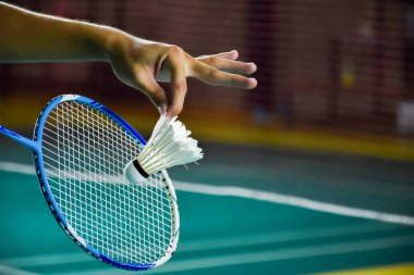 Badminton raketi ve eski beyaz mekikçik oyuncunun elinde tutarken ilerideki ağda servis yaparken, bulanık badminton sahası geçmişi ve seçici odaklanma.
