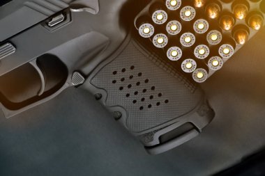 9mm 'lik tabanca ve siyah deri arka planda mermi kovanları, güneş ışığı düzenlenmiş, yumuşak ve seçici mermiler odaklı..