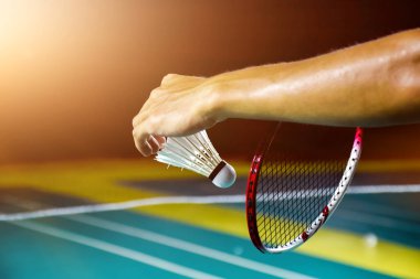 Badminton oyuncusu, badminton sahasının diğer tarafına atmadan önce beyaz badminton topu ve badminton raketini ağın önünde tutuyor. Beyaz mekikçik üzerine seçici odaklanma