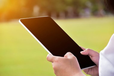 Asyalı kadınların ellerinde laplet, bulanık yeşil park geçmişi, günlük yaşamın her yerinde akıllı aletler kullanma konsepti. Lapete yumuşak ve seçici odaklanma.