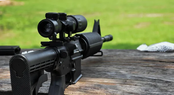 在训练场的木制桌子上有双筒望远镜的黑管长管自动步枪 也被称为空气软枪或Bb枪 软管和有选择的瞄准枪 — 图库照片