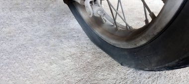 Düz ve kırsal yolun kenarındaki kaldırımda duran ve yeniden düzleştirilmeyi bekleyen bir motosiklet tekerleği. Yumuşak ve seçici odak.