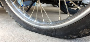 Düz ve kırsal yolun kenarındaki kaldırımda duran ve yeniden düzleştirilmeyi bekleyen bir motosiklet tekerleği. Yumuşak ve seçici odak.