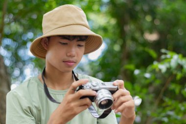 Kamerasını hazır tutan genç bir fotoğrafçı onu çevreleyen yemyeşil çevrenin güzelliğini çekmeye hazır..