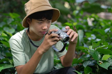 Kamerasını hazır tutan genç bir fotoğrafçı onu çevreleyen yemyeşil çevrenin güzelliğini çekmeye hazır..