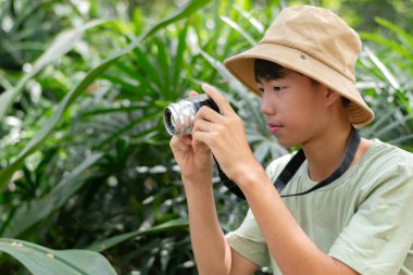Kamerasını hazır tutan genç bir fotoğrafçı onu çevreleyen yemyeşil çevrenin güzelliğini çekmeye hazır..