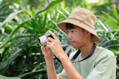 Kamerasını hazır tutan genç bir fotoğrafçı onu çevreleyen yemyeşil çevrenin güzelliğini çekmeye hazır..