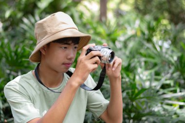 Kamerasını hazır tutan genç bir fotoğrafçı onu çevreleyen yemyeşil çevrenin güzelliğini çekmeye hazır..