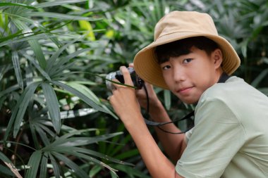 Genç bir fotoğrafçı aynasız kamerasını tropikal ormanın yemyeşil yaprakları arasında bir konuya doğrultur..