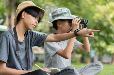 İki genç kâşif sahada işbirliği yapıyor, biri dürbünle gözlemlerken diğeri de bir defterde gördüklerini belgeliyor..