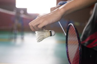 Badminton servisinin klasik duruşu, serbest kaldığında beyaz pipisi tutan oyuncunun elini göstermek, kırmızı çerçeveli raketin yeşil korta vurması için hazır olmak..
