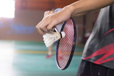 Badminton servisinin klasik duruşu, serbest kaldığında beyaz pipisi tutan oyuncunun elini göstermek, kırmızı çerçeveli raketin yeşil korta vurması için hazır olmak..