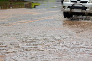 Koyu sarı taşkın suları kırsal bir yolu kaplayarak yolcuları engelliyor. Küresel ısınma, doğal afetler ve ormansızlaşmanın etkileri gibi çevre sorunları araç sigortasını etkileyebilir.