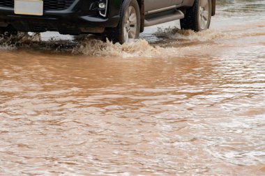 Koyu sarı taşkın suları kırsal bir yolu kaplayarak yolcuları engelliyor. Küresel ısınma, doğal afetler ve ormansızlaşmanın etkileri gibi çevre sorunları araç sigortasını etkileyebilir.
