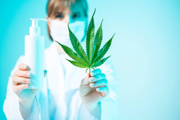 Modèle pot cosmétique blanc avec des produits du cannabis et de la feuille de chanvre dans les mains de scientifiques féminines dans la lumière au néon, gros plan — Photo