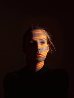 Karanlık stüdyoda yüzünde sıcak ışık olan güzel bir kızın yaratıcı portresi.