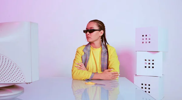 Стильна азіатська жінка-офіс працівник в сонцезахисних окулярах з застарілим комп'ютером за столом. Кольорове неонове світло — стокове фото