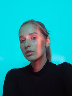 Mavi stüdyo arka planında yüzünde çapraz ışık olan havalı bir genç kız.