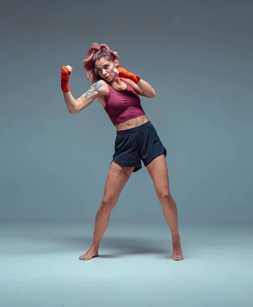 Lutador feminino treina em ataduras de boxe em estúdio em fundo cinza. — Fotografia de Stock