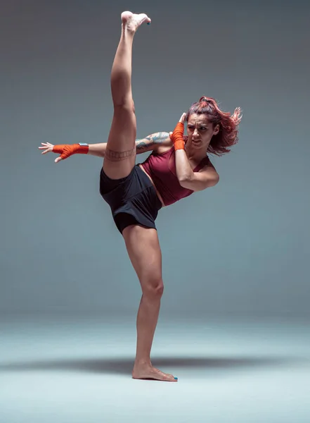 A young female fighter performs a high kick.