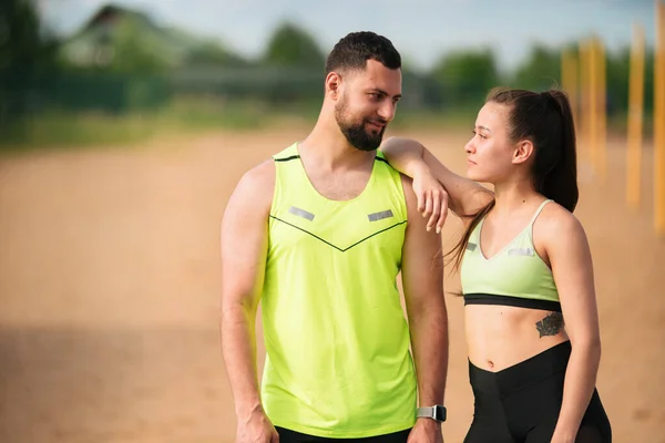 Cool athletic young couple in stylish sportswear having break after workout outdoor