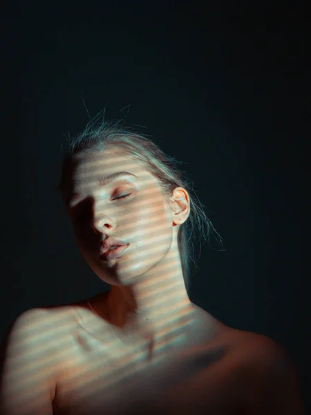 Estúdio retrato de menina bonita jovem com olhos fechados e ombros nus na escuridão com padrão de sombra na pele — Fotografia de Stock