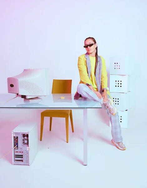 Antiguo ordenador y elegante mujer trabajadora creativa de oficina en gafas de sol con coletas sentadas en el escritorio. Luz de neón de color — Foto de Stock