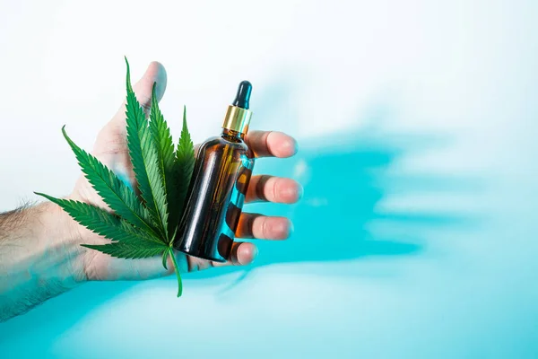 Hampa kosmetisk produkt i glasflaska och cannabis blad i manlig hand i neon ljus, ovanifrån. Naturlig hudvård — Stockfoto