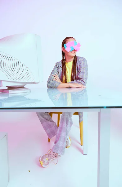 Stijlvolle vrouwelijke werknemer met stickers op het gezicht aan het bureau met oude computer monitor. Gekleurd Neon licht. Gekke kantoorsfeer — Stockfoto