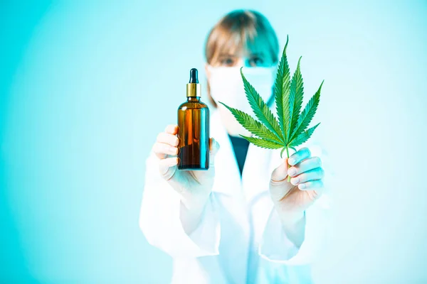 Produit de chanvre dans un bocal en verre et feuille de cannabis dans les mains de scientifiques féminines dans la lumière au néon — Photo