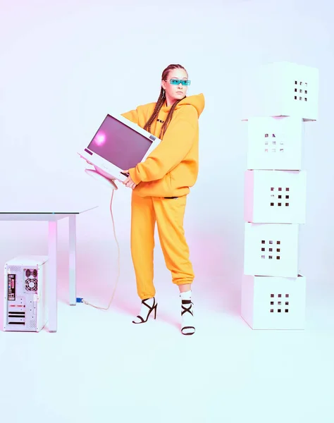 Cool female office worker in sunglasses standing with obsolete computer monitor and boxes. Colored Neon light