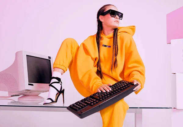 Stijlvolle vrouw in een zonnebril zittend met verouderde computer en toetsenbord op het bureau. Gekleurd neonlicht — Stockfoto