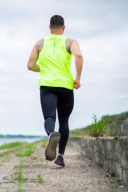 Şık spor kıyafetleriyle koşan atletik bir adam. Bulutlu bir havada, arka planda.