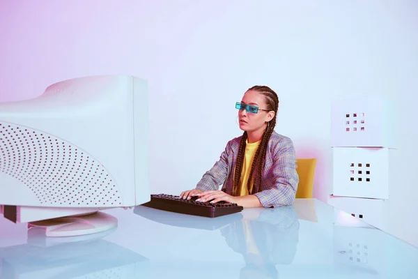 Aziatische vrouwelijke kantoormedewerker of hacker in zonnebril typen op oude computer. Gekleurd neonlicht — Stockfoto