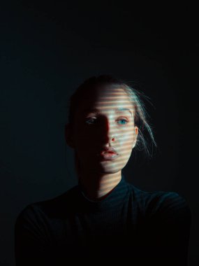 Karanlık stüdyoda yüzü gölgeli güzel bir genç kızın portresi.